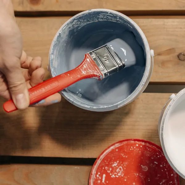 Mano sujetando una brocha mojada en pintura azul sobre un bote